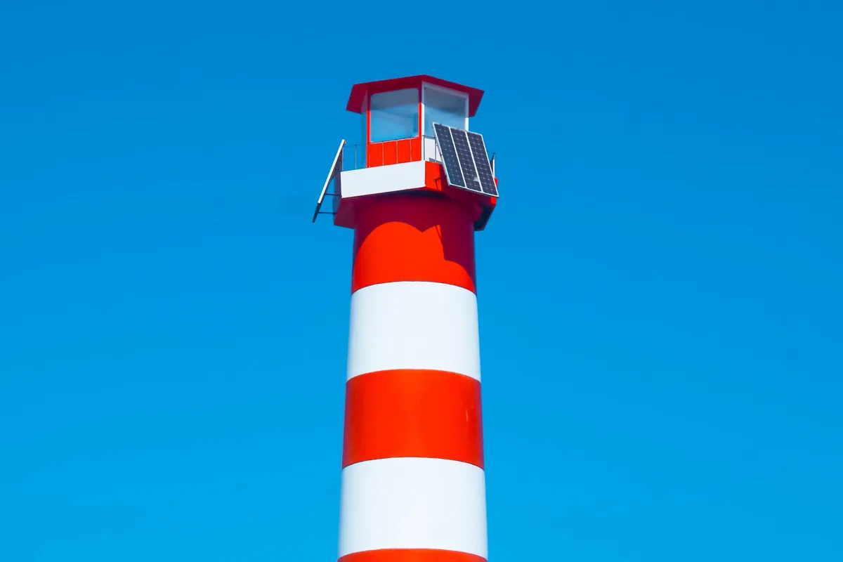 A red and white striped lighthouse standing against a clear blue sky