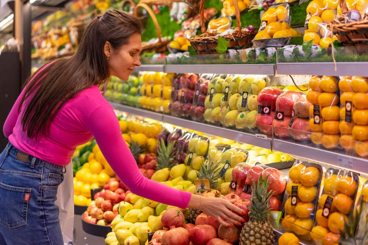 A woman in a bright pink top choosing fruit from a colourful market display