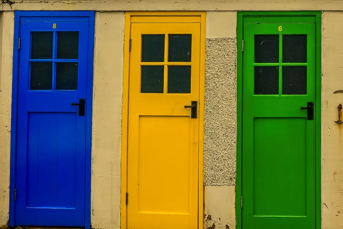 Three beach hut doors side by side, painted bright blue, yellow and green