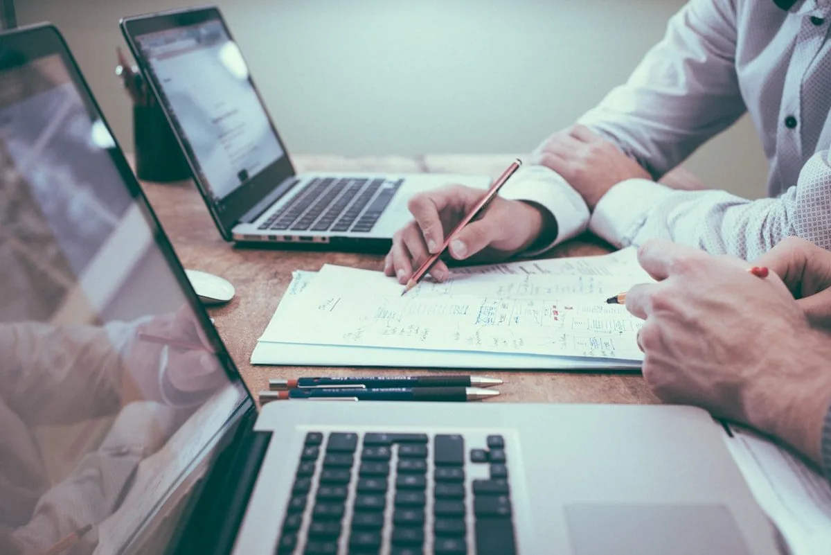 Hands reviewing documents beside a laptop