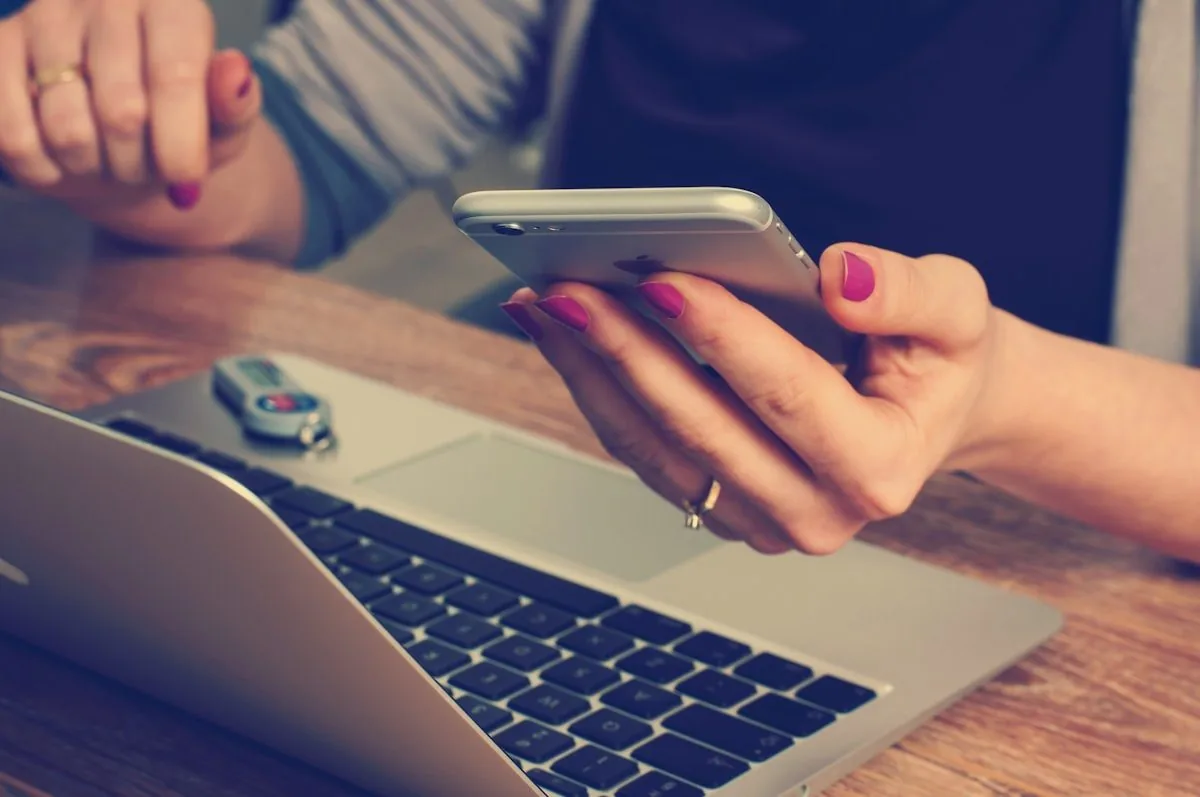 A hand holding a phone beside a laptop