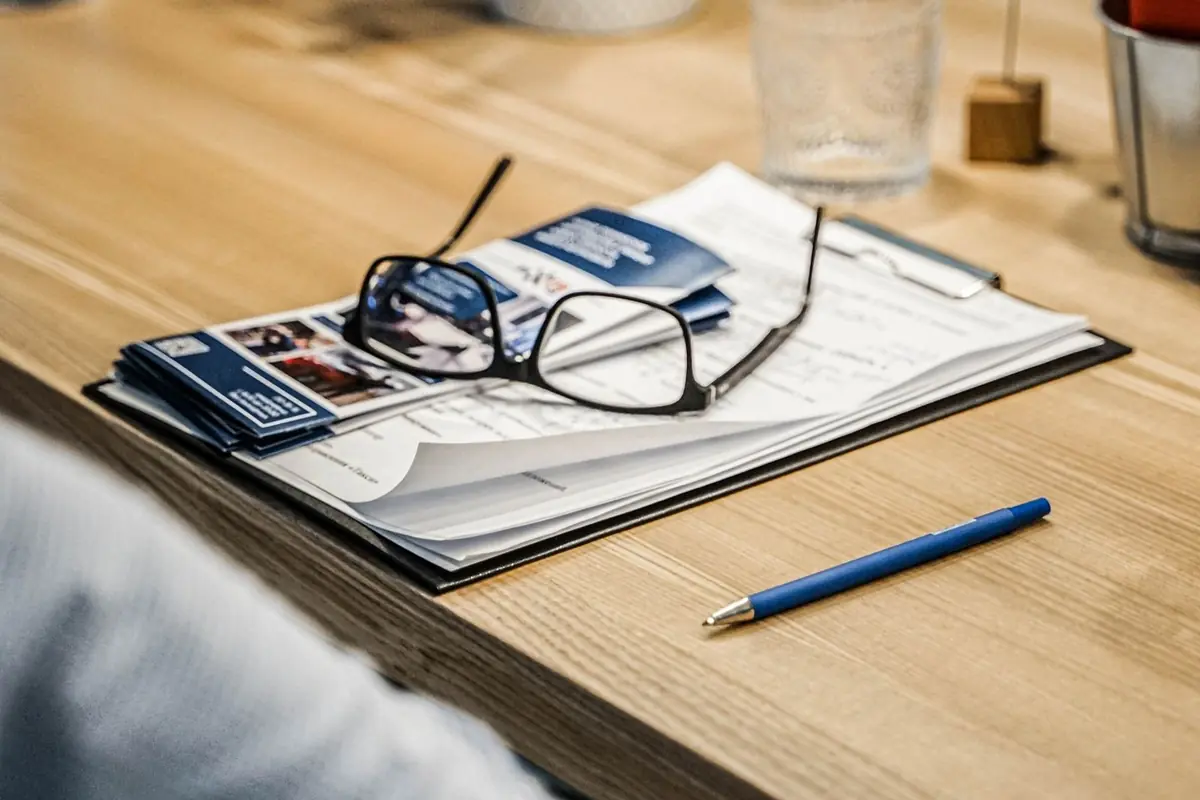 Eyeglasses resting on documents beside a pen