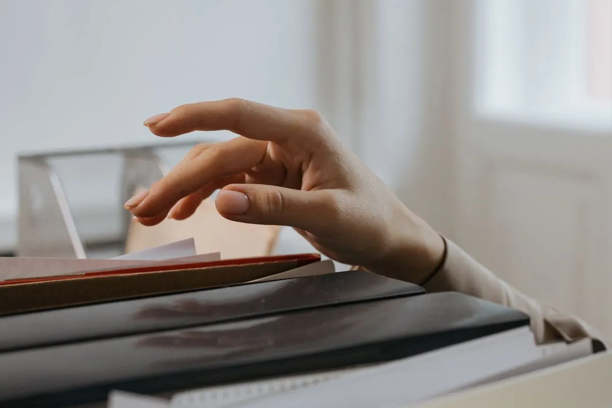A hand reaching over a stack of files and folders