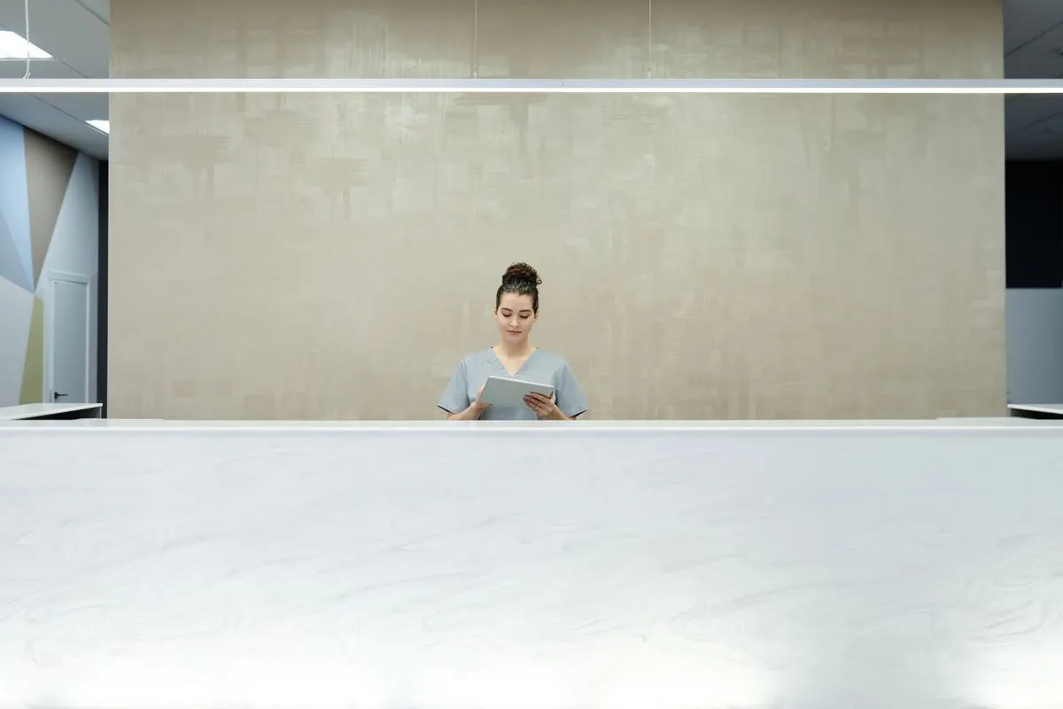 A receptionist at a long counter looking at a tablet