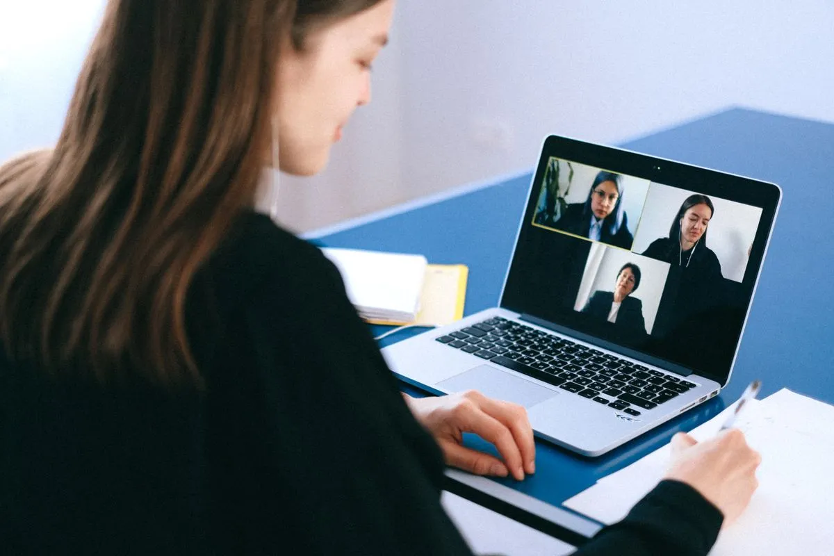 A woman taking notes during a video call on a laptop