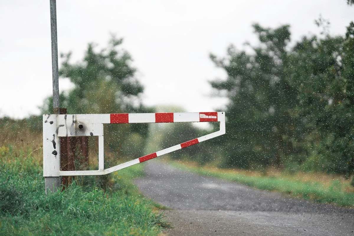 A white barrier gate closed across a country lane in the rain