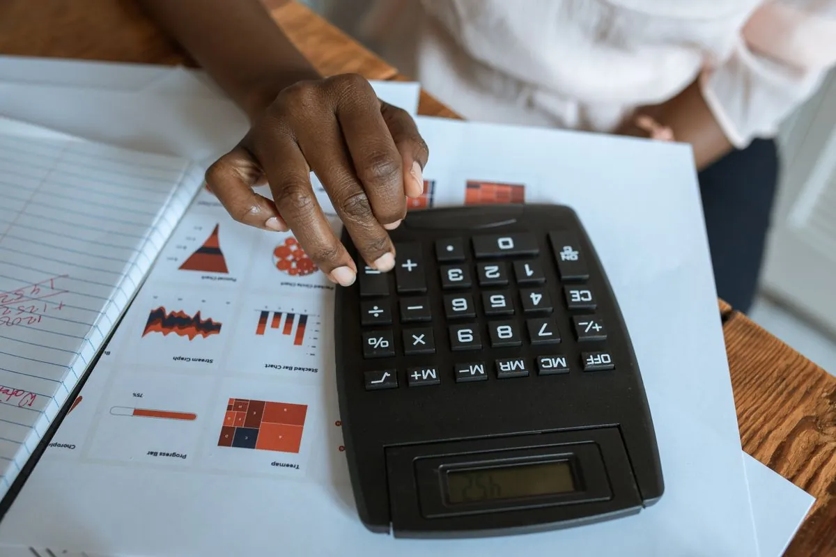 A woman at a wooden table working a calculator over a sheet of printed charts