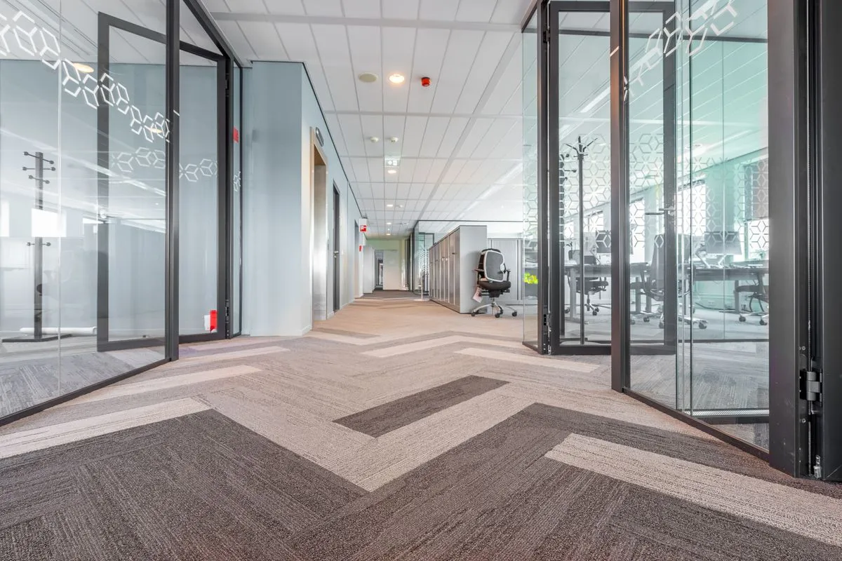 A bright office corridor with glass walled rooms and open glass doors