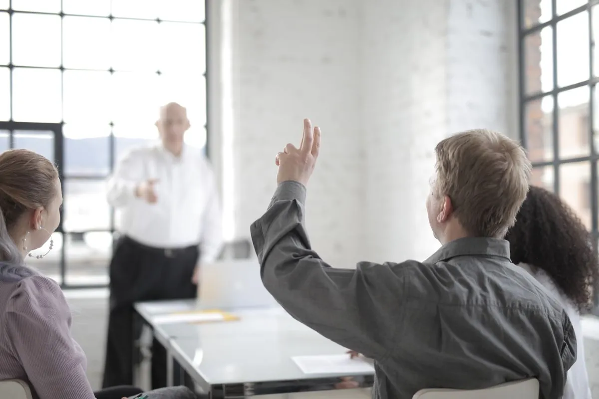 A raised hand at the back of a meeting room as a speaker takes questions
