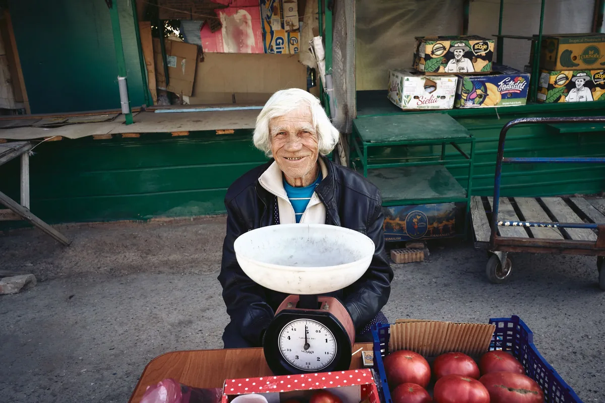 A stallholder smiling behind an old set of weighing scales on a colourful market stall