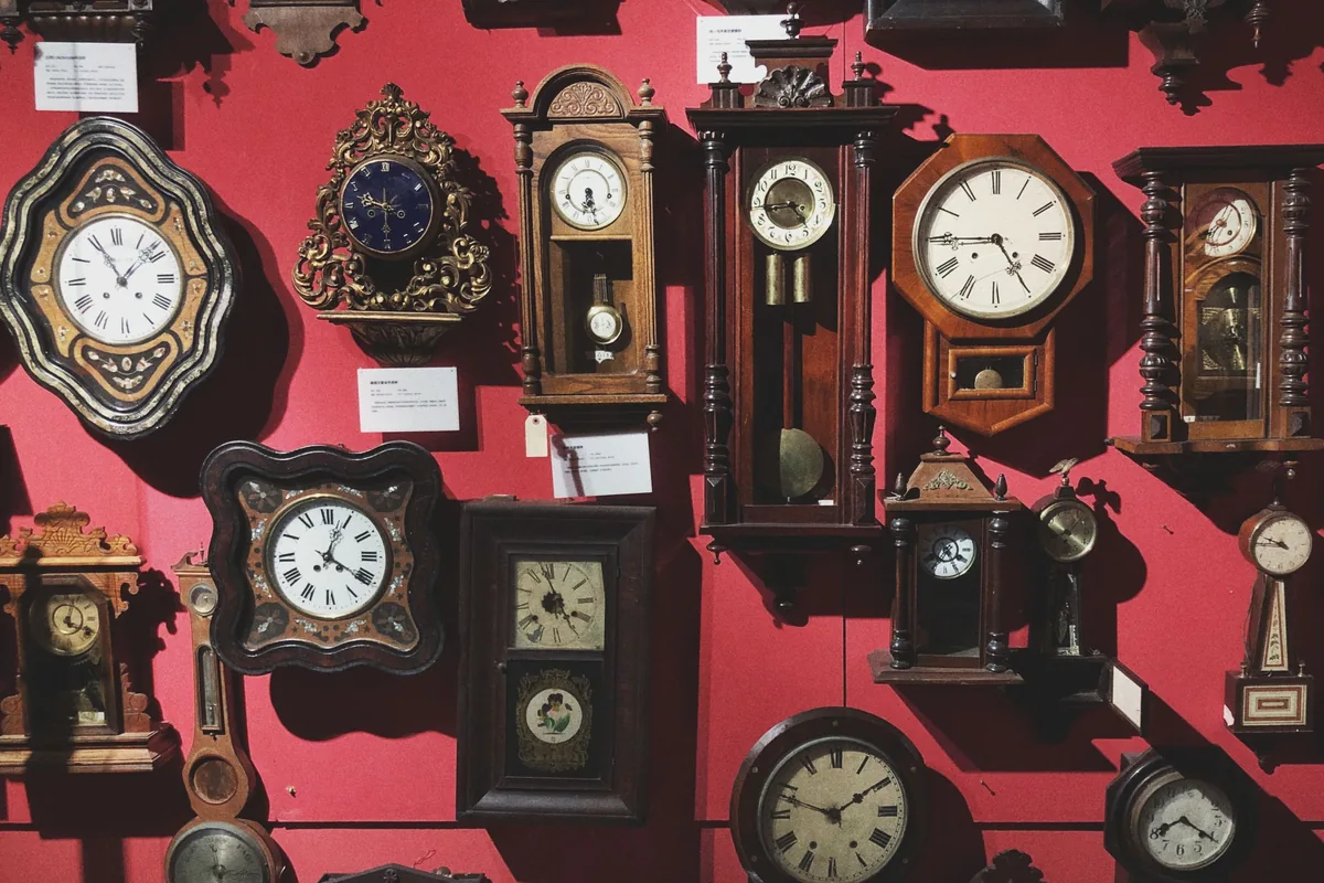 A wall of vintage clocks hung on a red background