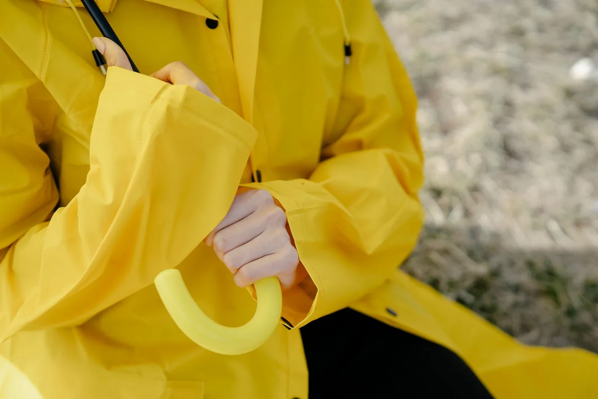 A person in a bright yellow raincoat gripping the hood against the weather