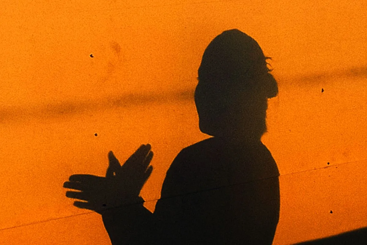 The shadow of a person clapping, cast across a bright orange wall