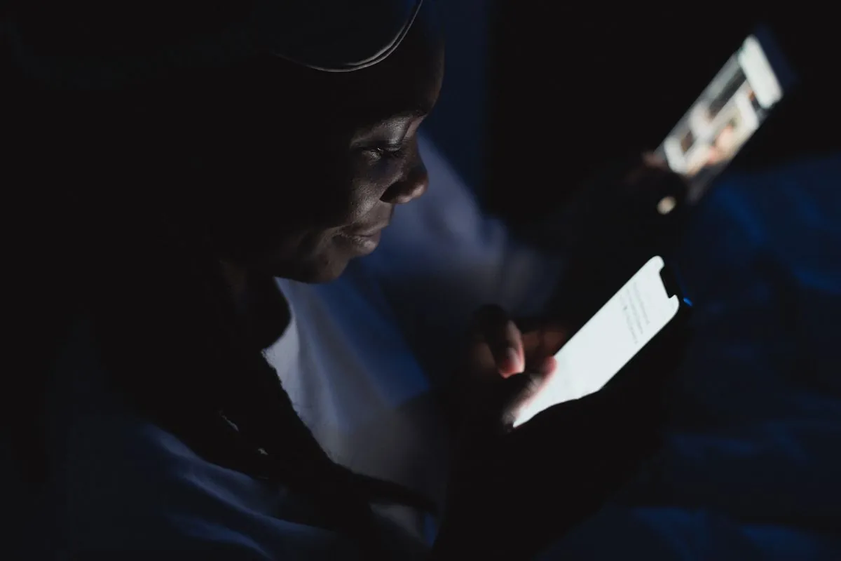 A person alone in a dark room at night, face lit by the screen of the phone they are reading